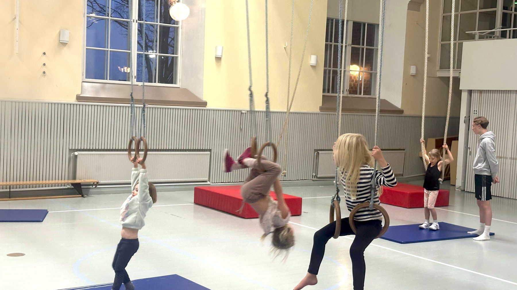 Lapsia liikuntasalissa temppuilemassa renkaissa